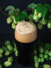 A glass of dark beer, craft stout or porter with green hop cones