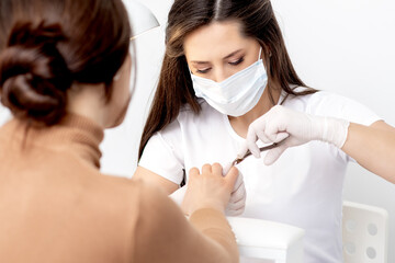 Manicurist in protective mask using manicure cutter to remove cuticle of female nails in manicure...