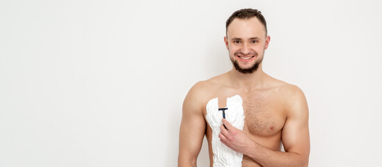 Young caucasian man with beard holds razor shaves his chest with white shaving foam on white...