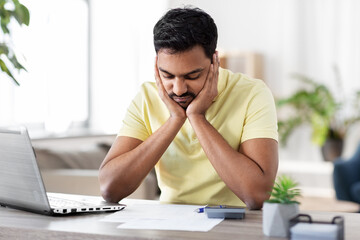 remote job, technology and people concept - unhappy young indian man with calculator and papers working at home office