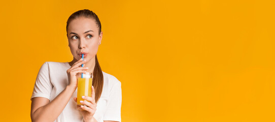 Pensive millennial girl drinking fresh orange vitamin juice with straw