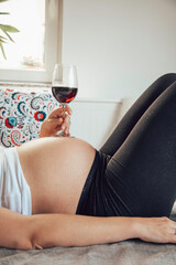 Pregnant woman holding a glass of wine on her belly.