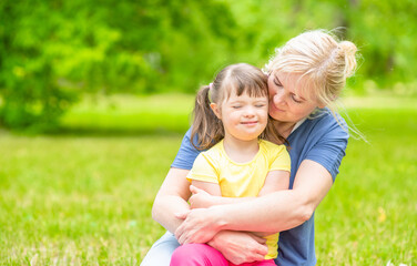 Happy little girl with syndrom down higs her mom in a summer park