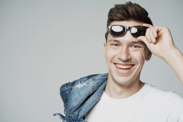 portrait of a cheerful young man of Caucasian appearance, holding sunglasses in his hands on his face. smiling funny joke shows teeth to a friend. the camera is watching.