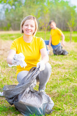 Smiling woman scavenges garbage in the summer park. Volunteer and ecology concept