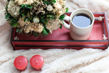 A Cup of coffee or tea, dry flowers and white, red candles, a red wooden box on a beige blanket