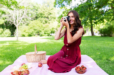 photography, leisure and people concept - happy smiling woman with camera, picnic basket sitting on...