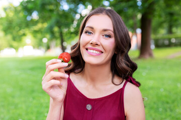 leisure and people concept - portrait of happy woman eating strawberry at summer park