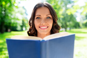Fototapeta premium leisure and people concept - happy smiling young woman reading book at summer park