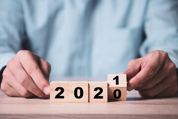 Businessman flipping wooden cubes block to change 2020 to 2021 year on wooden table. Happy new year and start new business concept.