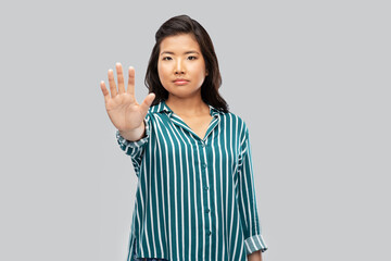 people, prohibition and rejection concept - asian young woman showing stop gesture over grey...