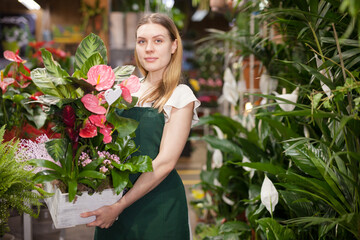 Cheerful woman florist holding pot with a flower in the gardening market. High quality photo