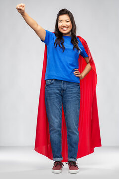 women's power and people concept - happy asian woman in red superhero cape over grey background