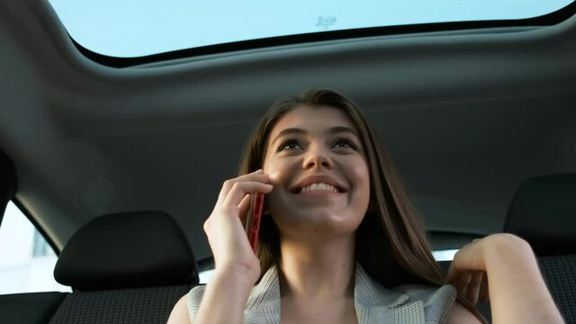 Beautiful business lady in a gray suit sits in a car with a panoramic roof and talks on the phone solving work moments