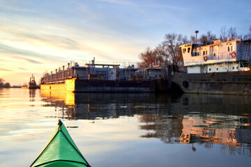 View from the green kayak on the old rusty ship. Danube river, autumn kayaking at sunset. Selective focus at kayak's prow.