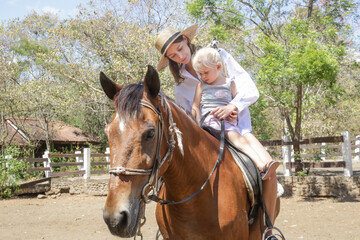 Beautiful young woman riding a horse with her little toddler girl, summer time outdoor activity
