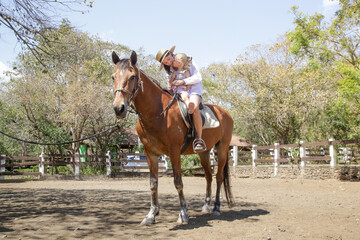 Obraz premium Beautiful young woman riding a horse with her little toddler girl, summer time outdoor activity