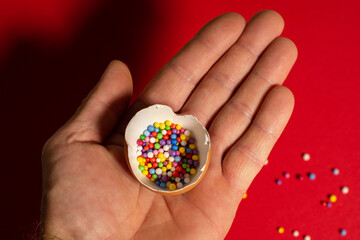 Man holding broken brown eggshell and bright foam balls on it