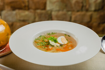 Fresh soup with vegetables, meat and eggs in a white plate.