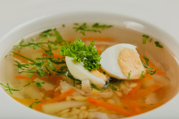 Fresh soup with vegetables, meat and eggs in a white plate.