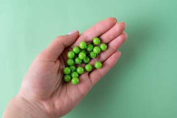 Girl hand hold coloured green pins for paper on green background. Minimalistic concept for school, business. Holding documents in office. Stationery stuff. Do not forget to pin something