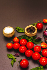 Ripe cherry tomatoes, garlic, basil, salt and black peppercorns on a black stone culinary background