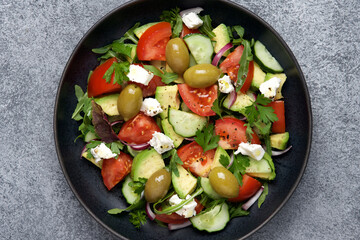 Greek salad with avocado. Tomatoes, cucumbers, olives, feta cheese fresh ingredients. Black background, top view