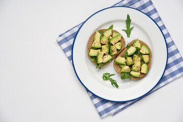 Avocado slices on whole grain bread with arugula. Healthy vegetarian breakfast concept. White background, top view