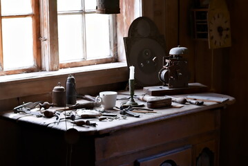 Clockmakers workshop with tools and clock parts strewn on the table with natural sunlight streaming in through the window.