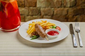 Freshly fried kebab with fried potatoes and tomato sauce on a white plate.