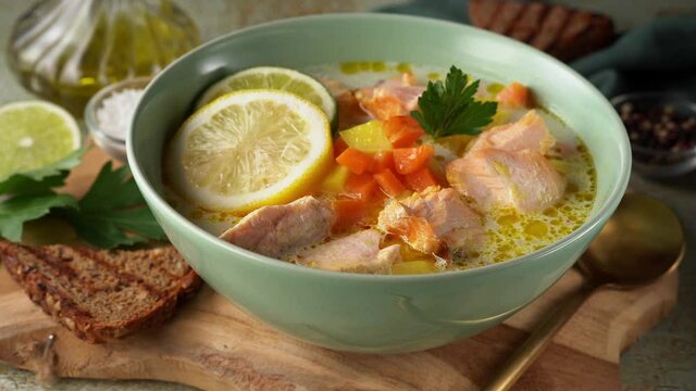 Woman hand placing a plate with healthy salmon fish soup on wooden board. 4K UHD