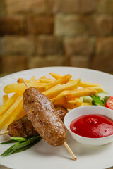 Freshly fried kebab with fried potatoes and tomato sauce on a white plate.