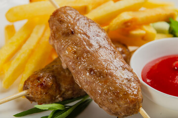 Freshly fried kebab with fried potatoes and tomato sauce on a white plate.