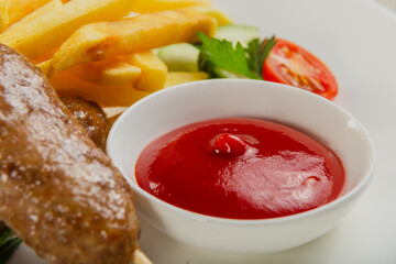 Freshly fried kebab with fried potatoes and tomato sauce on a white plate.