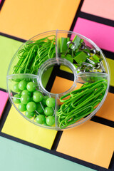 Green stationery set of pins, paper clips, binders, on coloured sticker notes background. Bright concept for school, business. Holding documents, papers in office. Stationery stuff. Selective focus.