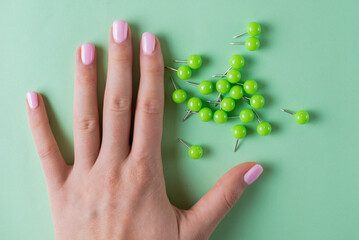 Girl hand near coloured green pins for paper on green background. Minimalistic concept for business, school. Holding documents in office. Stationery stuff. Do not forget to pin something