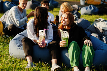 Young multi ethnic group of people watching movie at poof in open air cinema. Two girls with mojito cocktails.