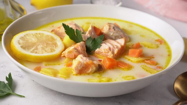 A side view of a plate with delicious and healthy salmon cream soup on white background. Close up. Movement from right to left