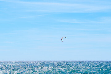 Kite surfing during holidays in a beautiful sunny day on the mediterranean sea or the ocean. Expressive sky with scattered smooth clouds. Solitary kite surfer, active lifestyle concept.