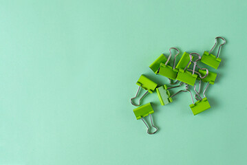 Bright green binder clip - office supply on green background. Minimalistic concept for school , business. Fasten documents or business papers in office. Coloured stationery stuff. Free space for text