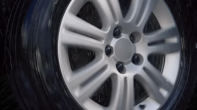 Car wheel with shiny silver rim rides in the rain drops, turns to the right. Closeup. Slow mo, slo mo, slow motion, high speed camera