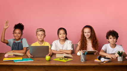 Focused black girl and her friends ready to answer lesson at desk over pink background, free space