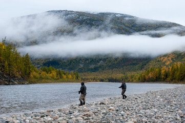Fisherman fishing by spinning on the shore of wild forest river.