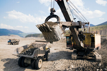 Excavator loads mountain soil into the bucket of a mining dump truck (gold mining industry)
