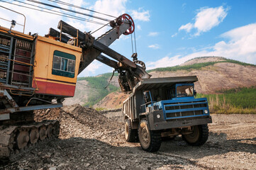 Excavator loads mountain soil into a dump truck bucket © Letopisec