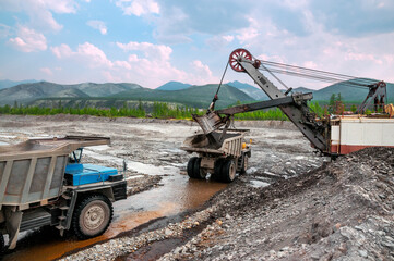  Loading of mountain earth soil into the side of a cargo mining dump truck by an excavator bucket in Eastern Siberia © Letopisec