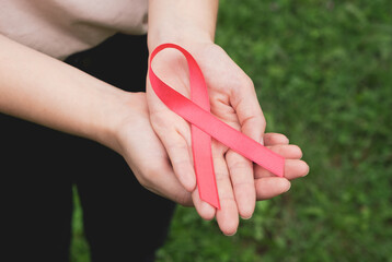 Womans hands hold pink breast cancer awareness ribbon. Medicine and womens health concept. Close up