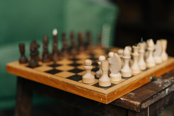 Side view of chessboard with placed chess pieces on black old vintage table, focus on foreground. End of preparation for an intellectual game in a warm home atmosphere.
