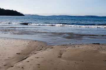 pristine beach in Tasmania with deep blue ocean and dark golden sand