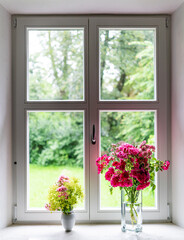 Rosenstrauß mit roten Rosen in Glasvase, auf Fensterbrett mit Blick hinaus in einen weiten Garten